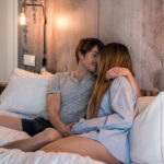 пара сидит на кровати в обнимку и целуется